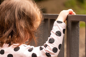 Little red-haired girl holding a turnstile in a summer park