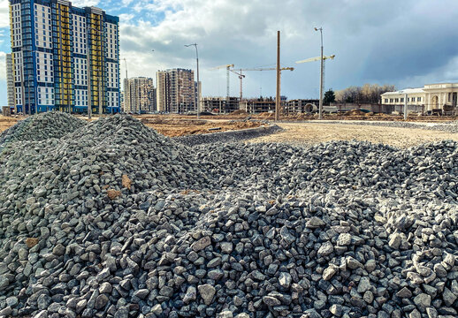 construction of a new microdistrict in the city center. tall, high-rise buildings made of concrete and glass next to a pile of stones. gray stones lie for the construction of the road