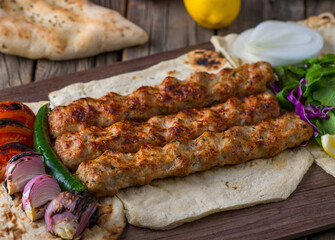 Chicken seekh kabab with onion ring, lime and tomato served in dish side view on wooden table background