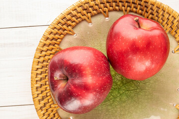 Two ripe red apples with a ceramic dish on a wooden table, close-up, top view.