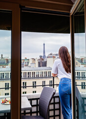 Back view of girl with long hair standing of balcony enjoying view at Eiffel Tower in Paris.