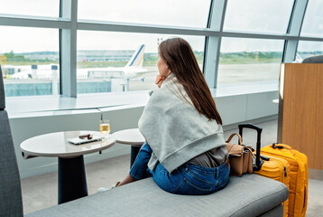 Young woman with yellow suitcase sitting in airport business lounge waiting for plane departure...