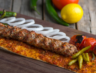 Chicken seekh kabab with onion ring, lime and tomato served in dish side view on wooden table background