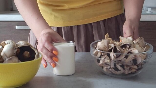 Woman cut mushrooms in champignons, prepared cream, milk and garlic to make cream soup, mashed soup or pasta sauce. Close up HD. Cooks lunch or dinner. Healthy protein vegetable food. Brown and yellow