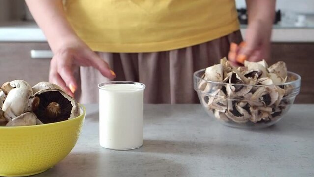 Woman cut mushrooms in champignons, prepared cream, milk and garlic to make cream soup, mashed soup or pasta sauce. Close up HD. Cooks lunch or dinner. Healthy protein vegetable food. Brown and yellow