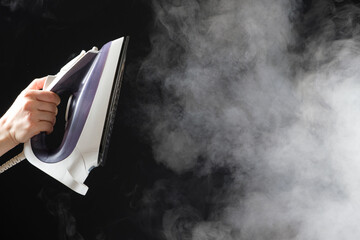 An iron with a steam generator sprays white hot steam on a black background. Steaming clothes,...