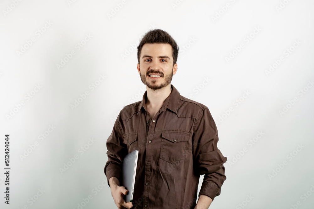 Wall mural Portrait of man wearing brown shirt posing isolated over white background holding in hands carrying laptop posing. Looking at the camera with big smiles.