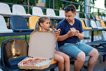 Father with daughter, soccer fans, watching football match, eating pizza and cheering for local...