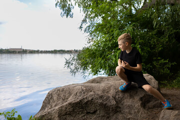 Naklejka na ściany i meble a boy looks into the river sitting on a stone