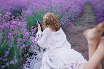 Teenage girl enjoys lavender field and makes photo with smartphone. Gen Z teenager with gadget...