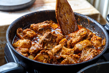 Chicken pieces stewed in pad thai sauce in spices in a deep frying pan with a wooden spatula.