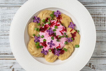 Appetizing dumplings stuffed with potatoes and mushrooms with sour cream decorated with beets and lilac flowers