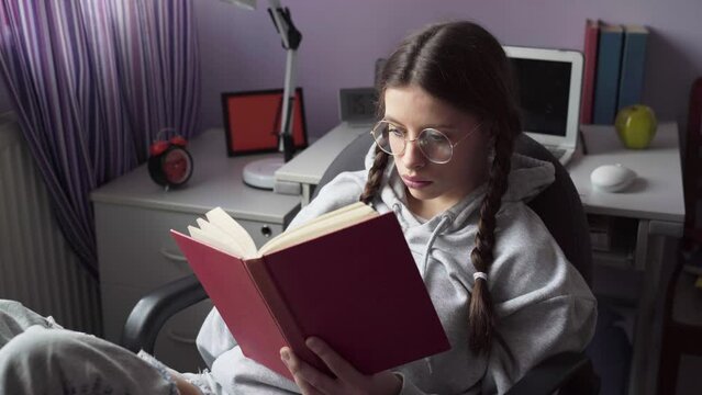 A student with glasses reads a school reading at home.