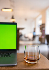 Cozy cafe atmosphere with a glass of coffee and a laptop with a green screen on the wooden table