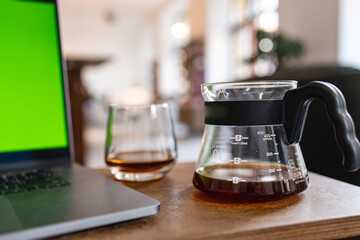 Cozy cafe atmosphere with a glass of coffee, carafe and a laptop with a green screen on the wooden table