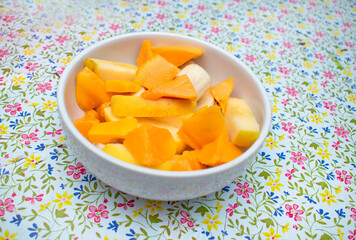 Plato de frutas entre ellas mango, manzana y platano en un mantel floreado