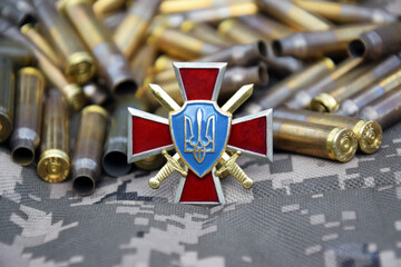 The badge of the ground forces of Ukraine against the background of military camouflage surrounded by shells.