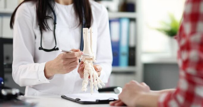 Doctor traumatologist shows model of a plastic leg of person to patient with problem with feet