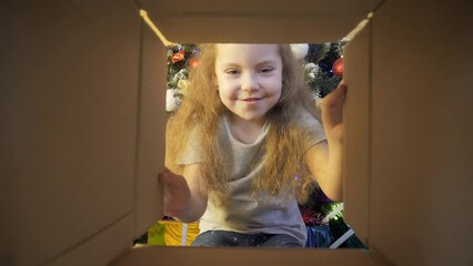 Opening a Christmas gifts. Happy little girl opens box with presents. A surprised child looks into the box with gifts near a decorated Christmas tree.