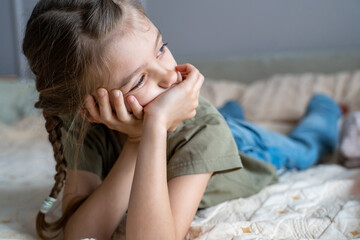 Cute little girl is lying on sofa with hands on chin, boring and looking out window