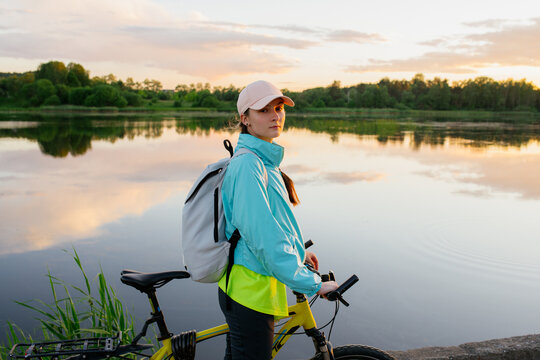 Nice woman riding mountain bike during sunset on the coastline above the lake. Bike travel tourism woman. Summer travel vacation recreation.