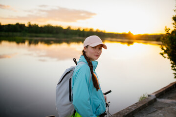 Traveling woman with backpack and hat looking at river at sunset. View from front tourist traveler bag. - 512433462