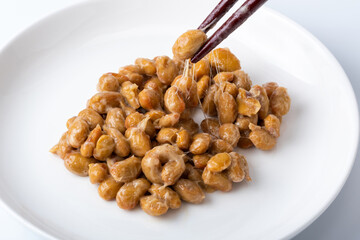 糸を引く納豆（小皿に乗せた丸大豆納豆を箸でつかむ）
