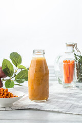 buckthorn smoothie or milkshake in a bottle with fresh berries on white wooden background