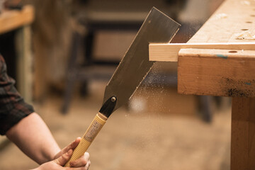 Unrecognizable male carpenter hands holding, sawing and using chisel , rasp with plank timber on...