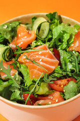 Fresh vegetable salad with salmon - tomatoes, avocado, cucumbers, and mix lettuce leaves.Fish salad. Healthy food. Isolated, orange background