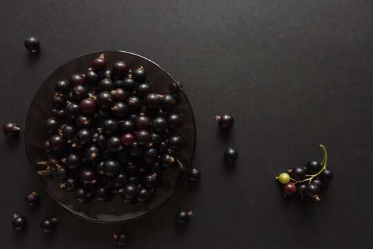 Ripe black currant berries in a glass plate on a black background. Top view. Food concept.