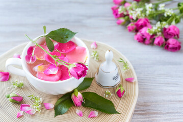 Tea of rose petal in a white cup, rose buds, bell on the wooden round tray. Rose` bouquet. Romantic mood. Post card