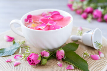 Obraz na płótnie Canvas Cup of tea with rose petals, rose buds, bell on the wooden round tray. Romantic mood. Post card