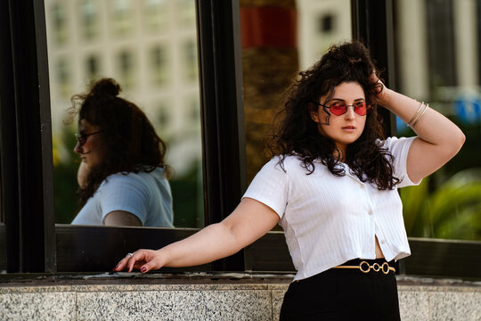 Photo of stylish young girl in fashionable sunglasses and clothes posing on the city street.