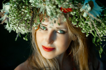 Beautiful girl with green eyes on her head a wreath of wild flowers