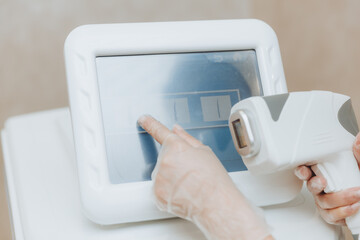 The beautician's hand presses the buttons on the device for laser hair removal. Close-up.Skin care equipment