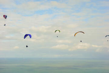colorful paragliders flying on cloudy sky above ocean