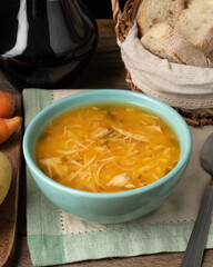 Chicken soup in a bowl with bread slices and wine over wooden table