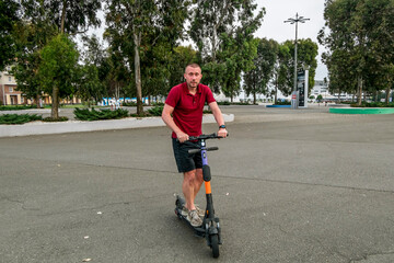 Attractive man riding a kick scooter at cityscape background.