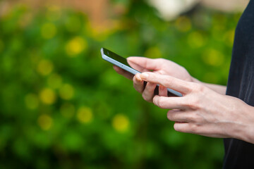 Holds a phone or device in his hands. Against the background of green vegetation.
