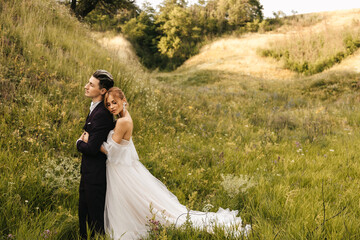 The bride hugs a stylish handsome groom. Beautiful couple in nature against the background of the hills