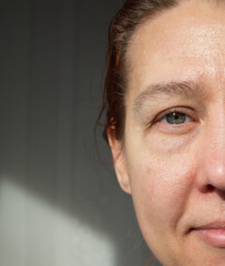 Close-up of half of the face of a happy mature middle-aged woman, a 50-year-old lady looks at the camera on a dark background. A busy life, a healthy lifestyle and positive emotions 