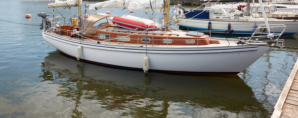 An elegant two masted sailboat (ketch) moored to a pier in a yacht marina. Wooden teak deck, rigging equipment, mast winch, ropes. Transportation, cruise, vacations, service and repair themes