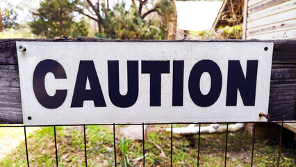 Caution Sign on a Wooden Fence with Black Letters
