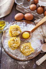 
Homemade pasta in the shape of nests on a wooden board with eggs, olive oil