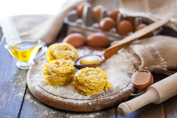 Fototapeta na wymiar Homemade pasta in the shape of nests on a wooden board with eggs, olive oil