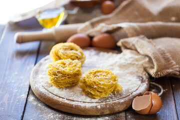
Homemade pasta in the shape of nests on a wooden board with eggs, olive oil