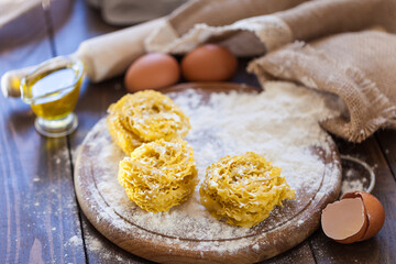 
Homemade pasta in the shape of nests on a wooden board with eggs, olive oil