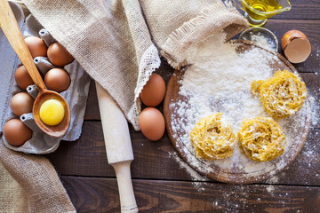 
Homemade pasta in the shape of nests on a wooden board with eggs, olive oil