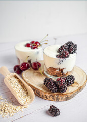 Yogurt with blackberries and cherries, fresh fruit with oat biscuit, white wood background.